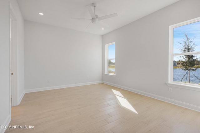 empty room featuring plenty of natural light, ceiling fan, a water view, and light wood-type flooring