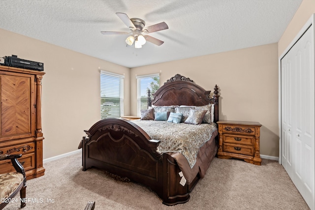 bedroom with a closet, ceiling fan, light colored carpet, and a textured ceiling