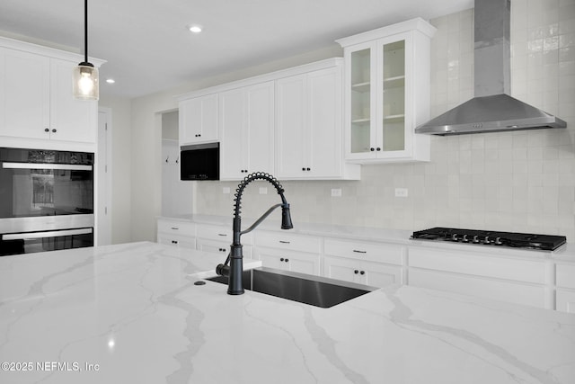 kitchen featuring light stone countertops, pendant lighting, sink, and wall chimney range hood