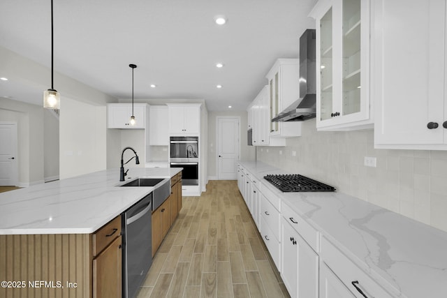 kitchen with wall chimney range hood, stainless steel appliances, light stone countertops, white cabinets, and decorative light fixtures