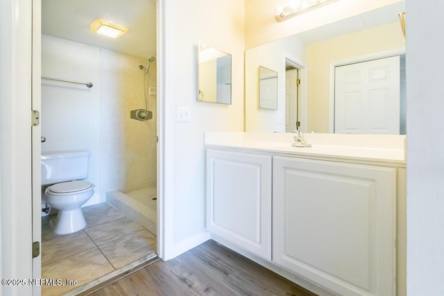 bathroom featuring a tile shower, hardwood / wood-style floors, toilet, and vanity