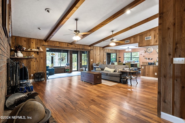 living room with wood walls, hardwood / wood-style flooring, ceiling fan, and lofted ceiling with beams