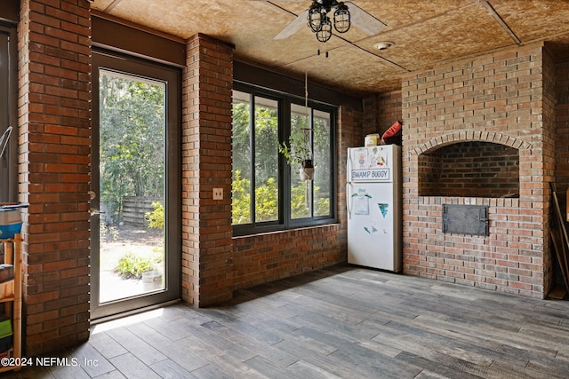 interior space featuring ceiling fan, hardwood / wood-style flooring, a healthy amount of sunlight, and brick wall