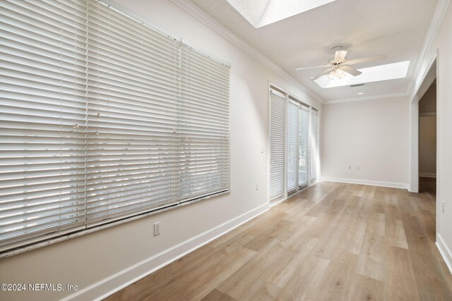 empty room featuring ceiling fan, a skylight, light hardwood / wood-style flooring, and ornamental molding