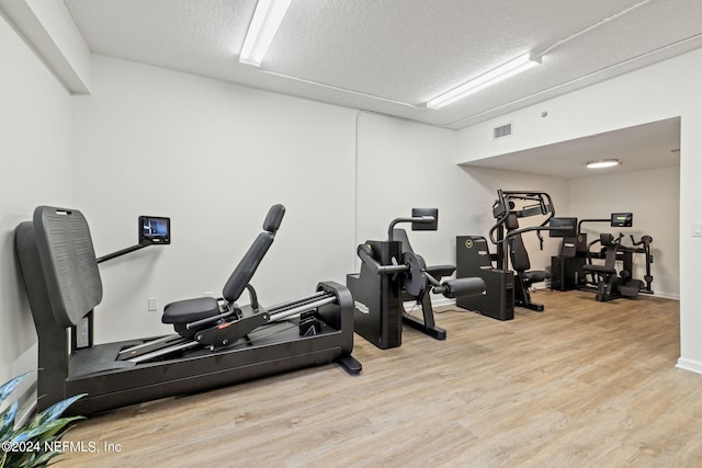 exercise room with a textured ceiling and light wood-type flooring