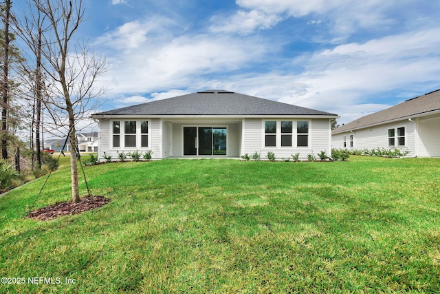 back of property with a shingled roof and a lawn