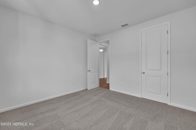 unfurnished bedroom featuring carpet floors, visible vents, a textured ceiling, and baseboards