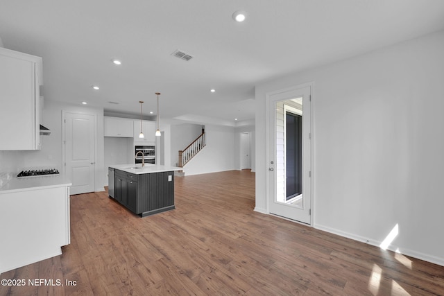 kitchen featuring hanging light fixtures, a kitchen island with sink, light countertops, white cabinetry, and a sink