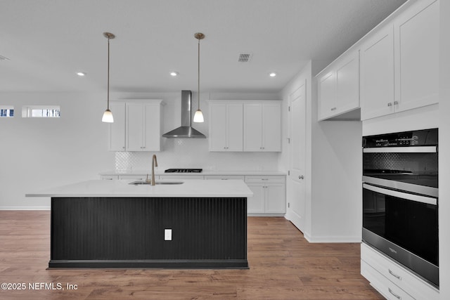 kitchen with light countertops, hanging light fixtures, white cabinetry, a sink, and wall chimney range hood