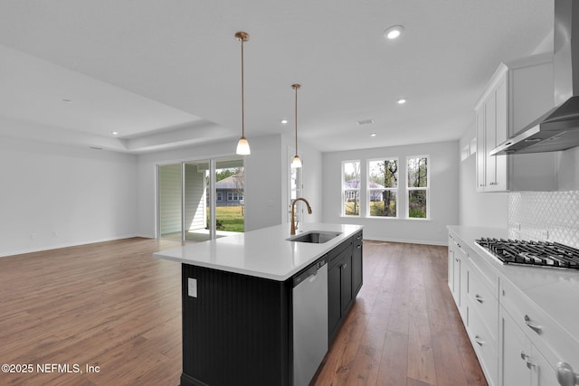 kitchen featuring wall chimney exhaust hood, a kitchen island with sink, appliances with stainless steel finishes, and light countertops