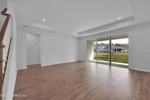 spare room with stairs, a tray ceiling, hardwood / wood-style floors, and baseboards