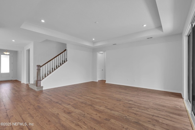 unfurnished living room with stairway, wood-type flooring, a raised ceiling, and recessed lighting