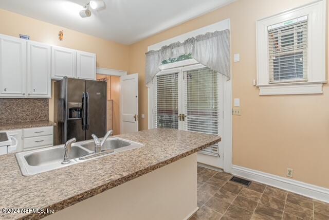 kitchen with decorative backsplash, white cabinets, black fridge, and sink