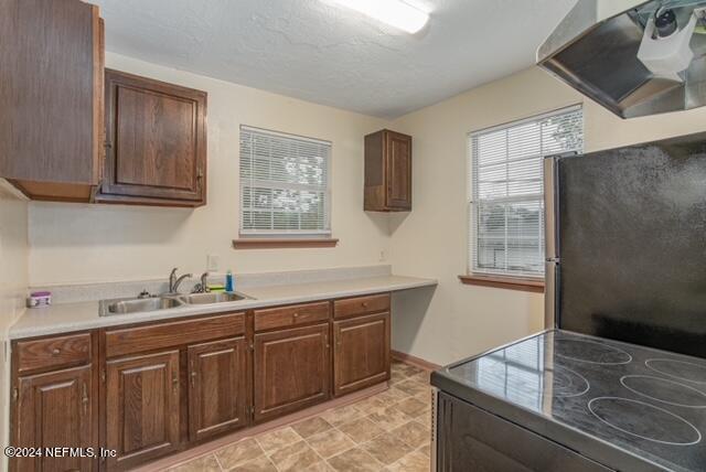 kitchen with ventilation hood, a textured ceiling, stove, sink, and black fridge