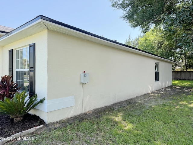 view of side of property featuring fence, stucco siding, and a yard