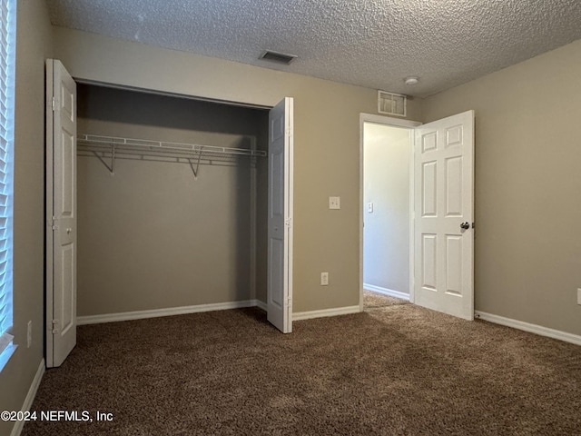 unfurnished bedroom with a textured ceiling, dark colored carpet, and a closet