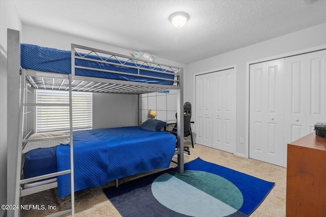 bedroom with a textured ceiling, two closets, and carpet flooring