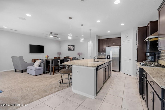 kitchen featuring ceiling fan, sink, a kitchen island with sink, stainless steel appliances, and light carpet