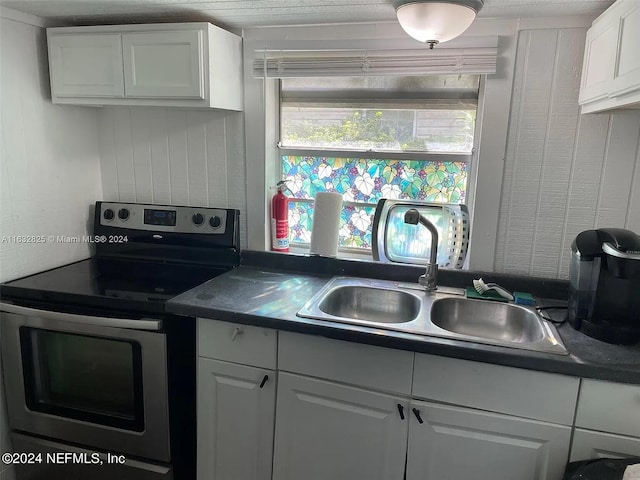 kitchen with stainless steel electric range oven, sink, and white cabinetry