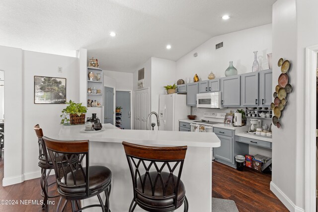 kitchen with lofted ceiling, kitchen peninsula, white appliances, a breakfast bar, and dark hardwood / wood-style flooring