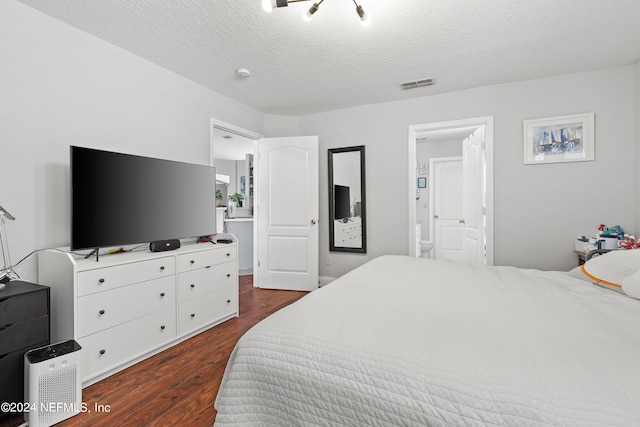 bedroom with a textured ceiling, connected bathroom, and dark hardwood / wood-style flooring