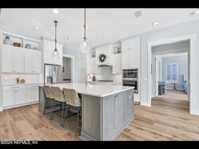 kitchen featuring stainless steel appliances, white cabinetry, a center island with sink, and light hardwood / wood-style floors