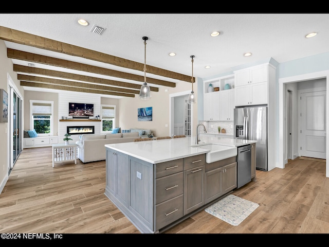 kitchen with beamed ceiling, sink, white cabinetry, stainless steel appliances, and a fireplace