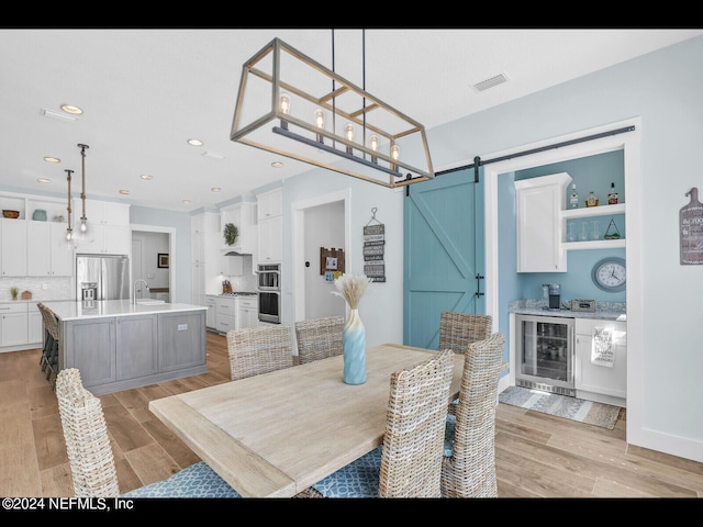 dining area featuring wine cooler, light hardwood / wood-style floors, and a barn door