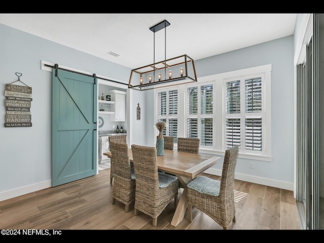 dining space featuring a barn door, a textured ceiling, a notable chandelier, and hardwood / wood-style flooring