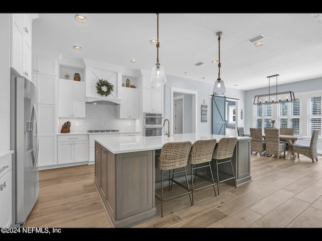 kitchen featuring pendant lighting, a center island with sink, light hardwood / wood-style flooring, white cabinetry, and stainless steel appliances