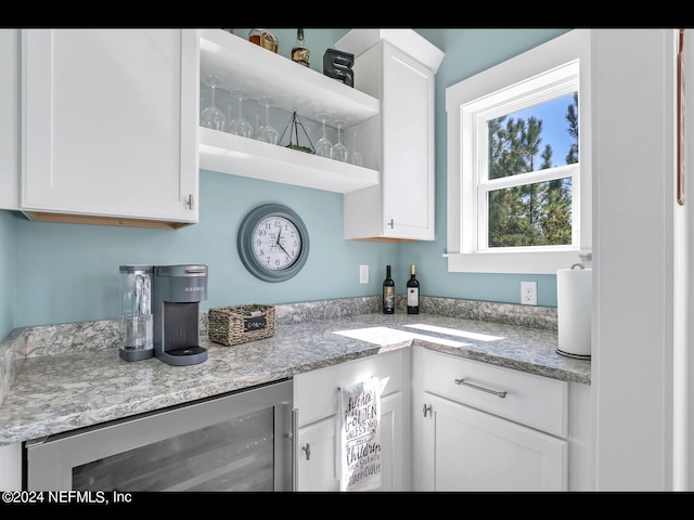 kitchen featuring beverage cooler, white cabinetry, and light stone counters