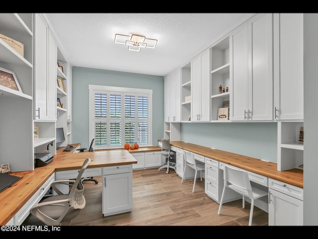 home office with built in desk, a textured ceiling, and light wood-type flooring