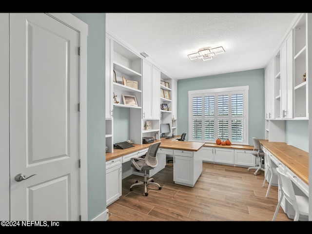 office space featuring a textured ceiling, light hardwood / wood-style flooring, and built in desk