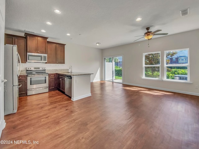 kitchen with appliances with stainless steel finishes, kitchen peninsula, a textured ceiling, ceiling fan, and hardwood / wood-style floors