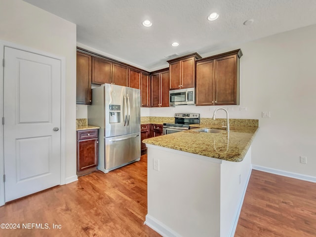 kitchen featuring stainless steel appliances, light stone counters, light wood-type flooring, and sink