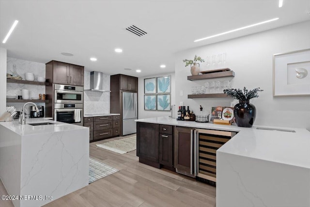 kitchen featuring light hardwood / wood-style floors, sink, kitchen peninsula, wall chimney exhaust hood, and appliances with stainless steel finishes