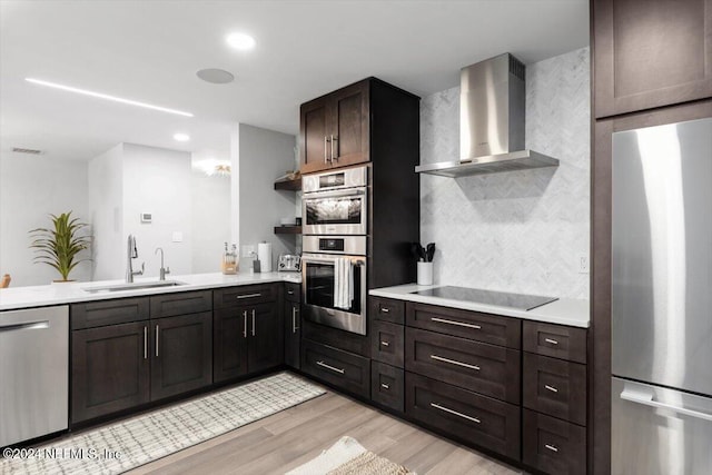 kitchen featuring sink, dark brown cabinets, wall chimney exhaust hood, stainless steel appliances, and light wood-type flooring