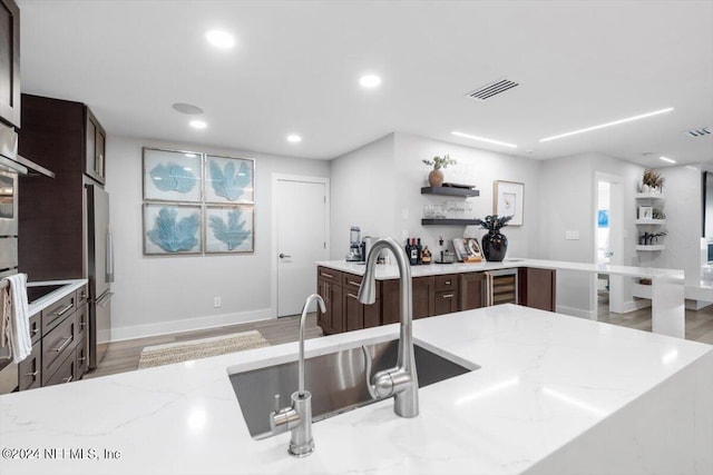 kitchen featuring light wood-type flooring, light stone counters, sink, and stainless steel fridge