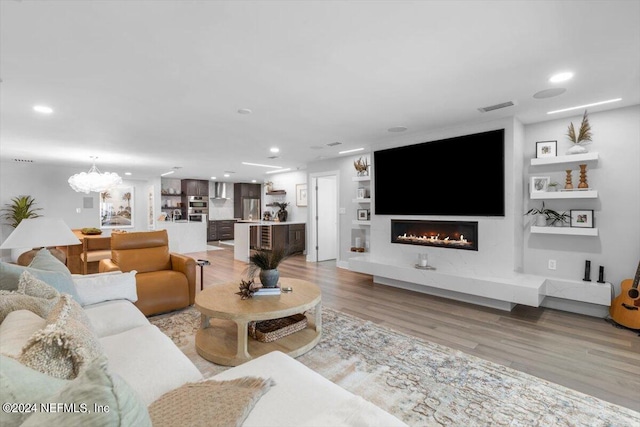 living room with a notable chandelier, built in shelves, and light hardwood / wood-style floors