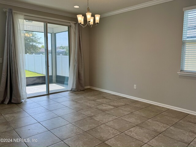 tiled empty room with a healthy amount of sunlight, crown molding, and an inviting chandelier