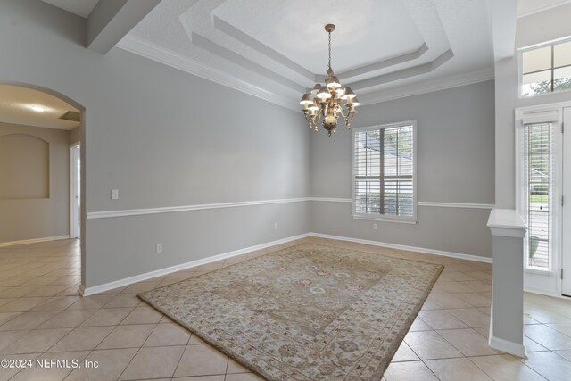 tiled spare room with an inviting chandelier, a tray ceiling, a healthy amount of sunlight, and crown molding