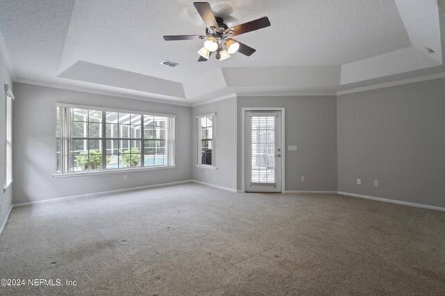 carpeted spare room with ceiling fan, a tray ceiling, plenty of natural light, and crown molding