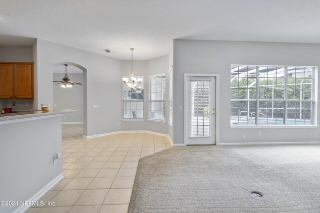 interior space with ceiling fan with notable chandelier, a wealth of natural light, a textured ceiling, and light tile patterned floors