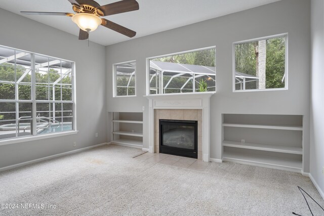 unfurnished living room with ceiling fan, light colored carpet, a tiled fireplace, and a healthy amount of sunlight