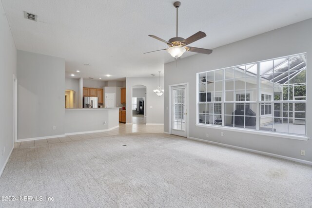 unfurnished living room featuring ceiling fan with notable chandelier and light carpet