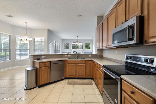 kitchen with pendant lighting, light tile patterned floors, sink, appliances with stainless steel finishes, and an inviting chandelier