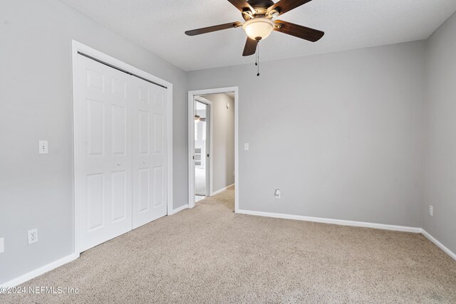 unfurnished bedroom with a closet, ceiling fan, light colored carpet, and a textured ceiling