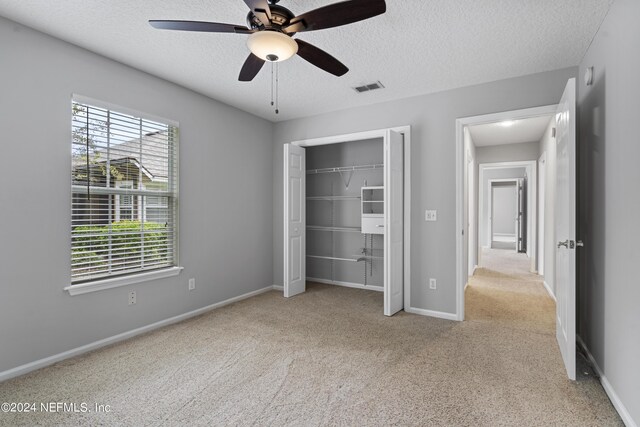 unfurnished bedroom with a closet, ceiling fan, light colored carpet, and a textured ceiling