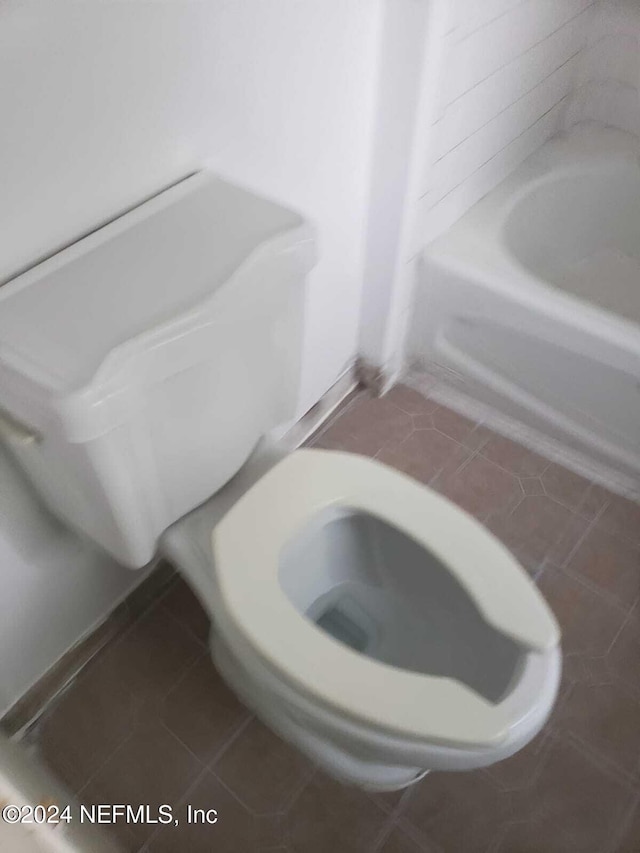 bathroom with tile patterned flooring, a tub to relax in, and toilet