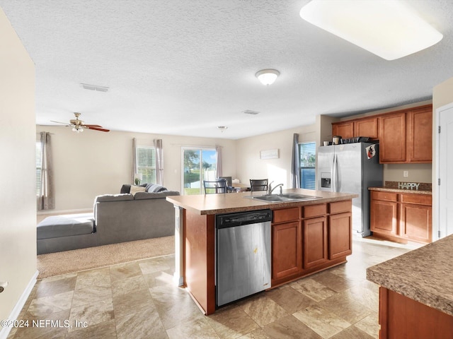 kitchen with a textured ceiling, appliances with stainless steel finishes, sink, and an island with sink